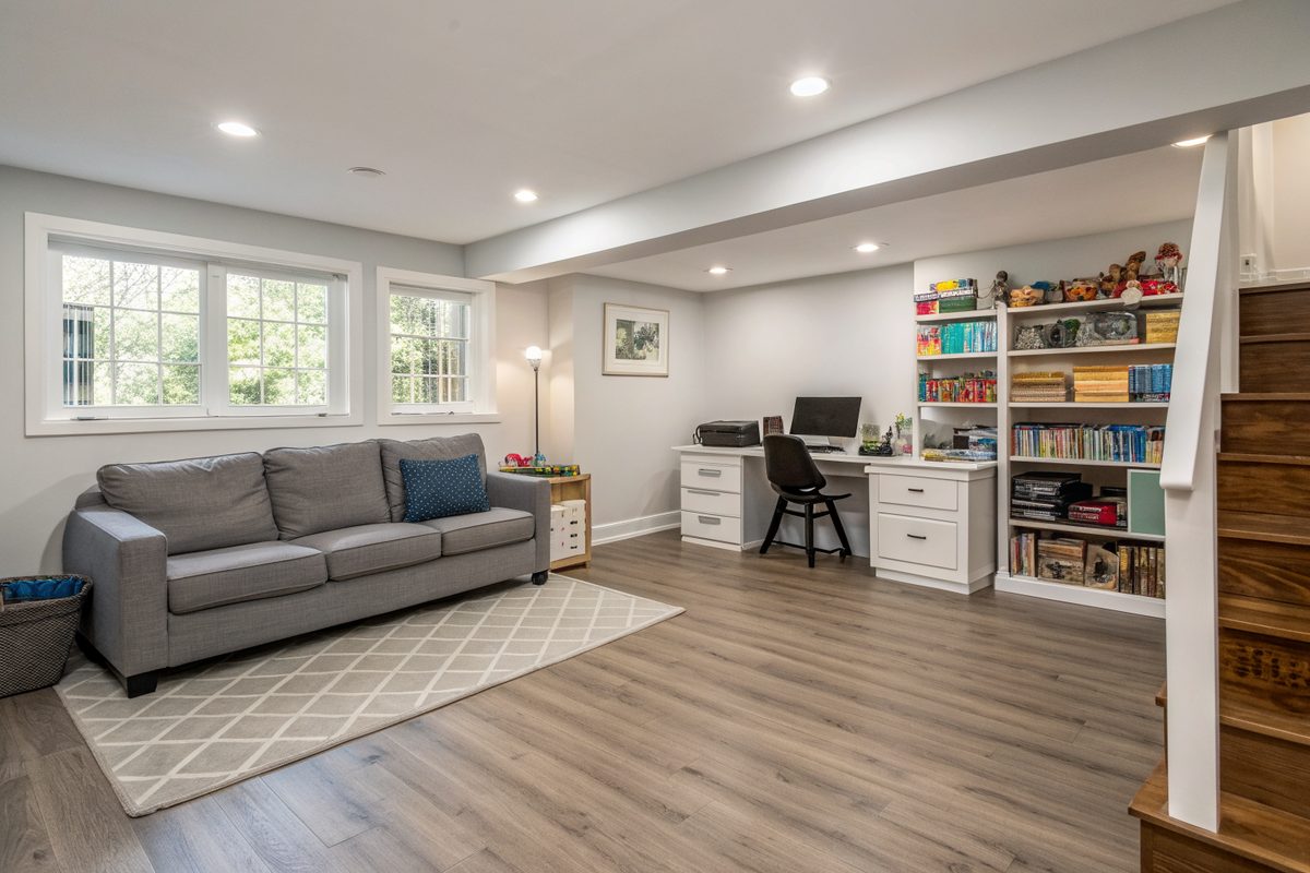 A dry finished basement office and play area with plank flooring, a gray couch and shelves